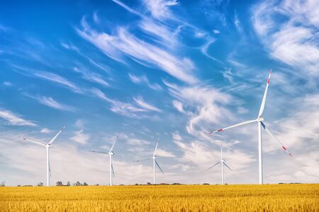 Wind power plant in the yellow field against cloudy sky. Bright autumn landscape