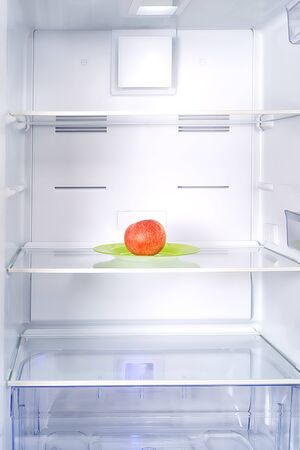 Empty fridge with single red apple inside. Dieting and lack of food themeの写真素材