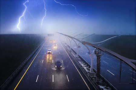 Cars driving on a highway in a pouring rain with a thunderstorm. Storm, lightning and fog over dark...