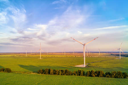 Wind power plant in the green field against cloudy sky at sunset. Panoramic aerial view
