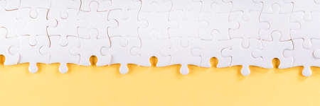 Assembled white jigsaw puzzle pieces on yellow. Long panoramic texture and background