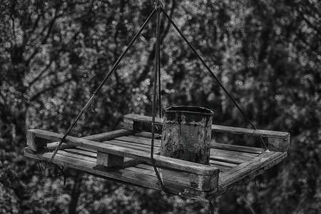 Old bucket on a wooden suspended platform against a lush foliage. Overhaul, construction works and obsolete equipment theme. Low key black and white photoの写真素材