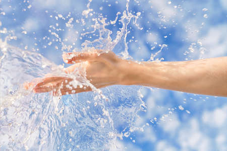 Woman hand with large water splash in it against blue sky. Bright summer image, nature and ecology themeの写真素材