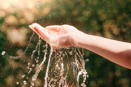 Woman hand with water splash in it against defocused brown toned foliage. Toned water, nature and ecology theme image with selective focusの写真素材