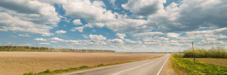 Endless country road to the horizon, fields and forest under cloudy sky. extra wide panoramic viewの写真素材