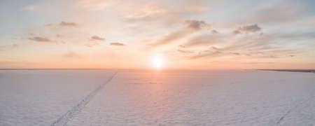 Ice on the frozen sea and bright colored sky at sunset. Aerial long panoramic view, one point perspectiveの写真素材