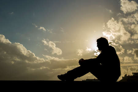 Sad young man silhouette worried on the stone at sunset, Silhouette conceptの写真素材