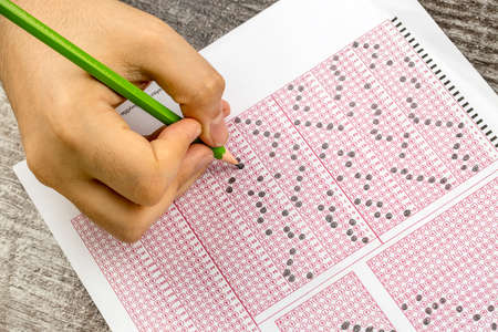 Students hand doing exams quiz test paper with pencil drawing selected choice on answer sheets at schoolの写真素材