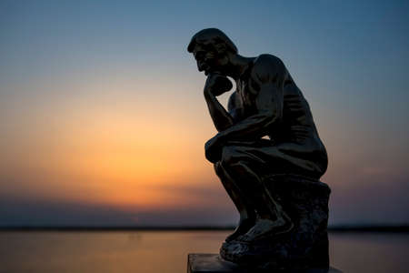Sculpture thinking man in sunset silhouette. Concept photo.
