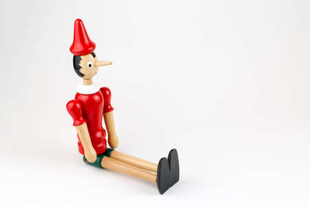 Wooden Pinocchio doll sitting isolated on white background.の写真素材