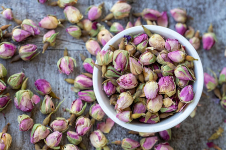 Dried rose buds in a white bowl on a wooden table.の写真素材
