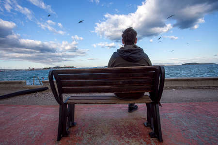 A man sits on a bench by the sea and looks into the distance.の写真素材