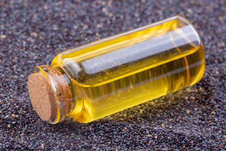 poppy oil in a glass bottle on a background of poppy seedsの写真素材