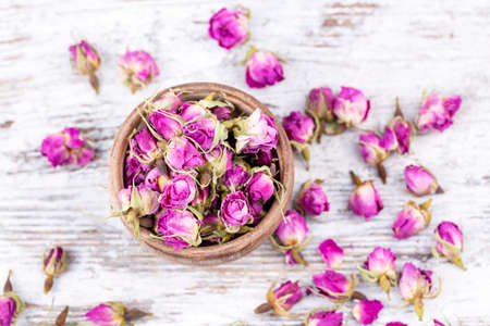 Dried rose buds in bowl on wooden background. Top view.の写真素材
