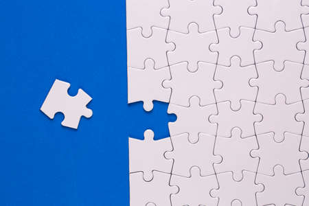 Missing jigsaw puzzle pieces. Business concept. Fragment of a folded white jigsaw puzzle and a pile...