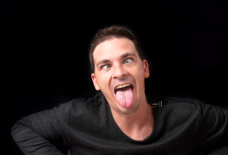 Young man sticking out his tongue. Isolated on black background.の写真素材