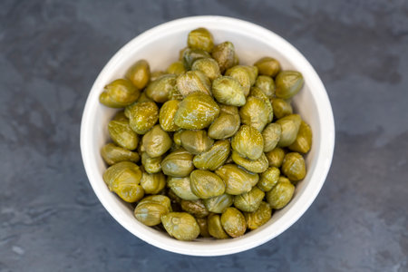Pickled capers in a glass bowl on a dark background, top view close up (Turkish name; capers)の写真素材