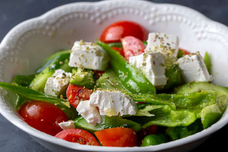 Greek salad with feta cheese, cherry tomatoes, cucumbers and green onions in a white plate on a dark background.の写真素材