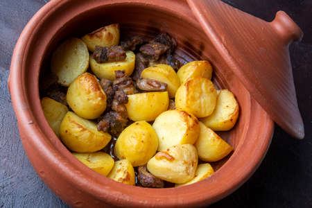 Fried potatoes with meat and spices in a clay pot on a dark backgroundの写真素材