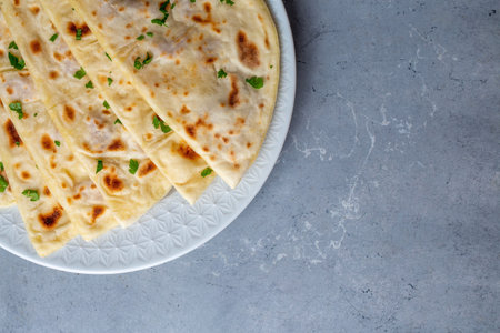 Traditional Turkish D-shaped flatbread gozleme with fresh parsley served on a white plate over gray marble background.