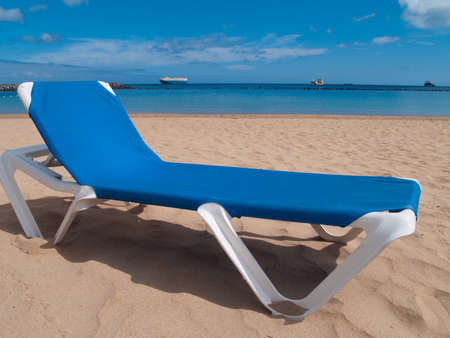 vacation concept: beach chairs on white sand on the shore of ocean