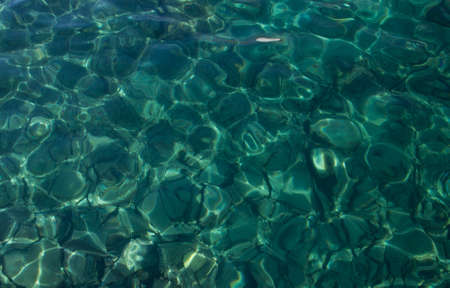 sea water with sunlight on turquoise pebbles background 