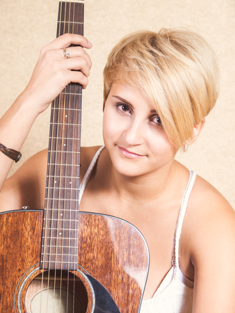 Young girl in jeans and white blouse sits on a floor with the guitarの写真素材