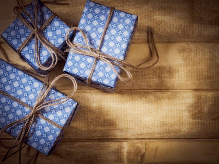 Top view of gift boxes in blue paper decorated with linen cord on the wooden table. Dark toned