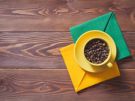 Coffee cup with coffee beans and yellow and green napkins on the wooden table. Top viewの写真素材