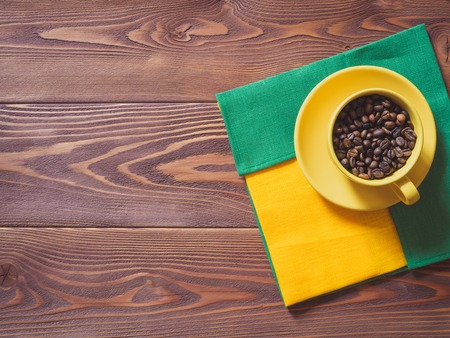 Coffee cup with coffee beans and yellow and green napkins on the wooden table. Top viewの写真素材