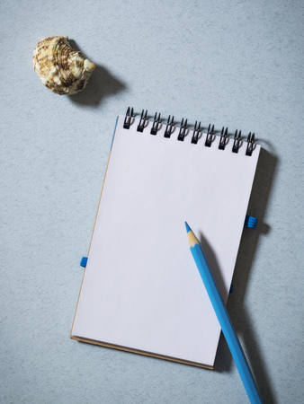 Notebook, pencil and seashell on the tableの写真素材