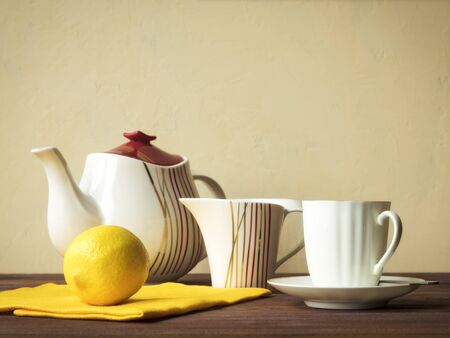 Teapot, cup with saucer, milk jug and lemon on the wooden tableの写真素材
