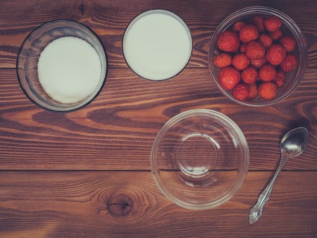 Summer breakfast. Glass of milk, pialat with strawberries and sugar-bowl on the wooden table. Dark tonedの写真素材