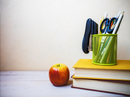 View on the pile of books, apple and cup with pencils lying on the wooden tableの写真素材