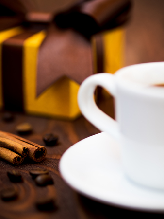Cup of coffee, cinnamon sticks and coffee beans on the table with the wrapped gift boxの写真素材