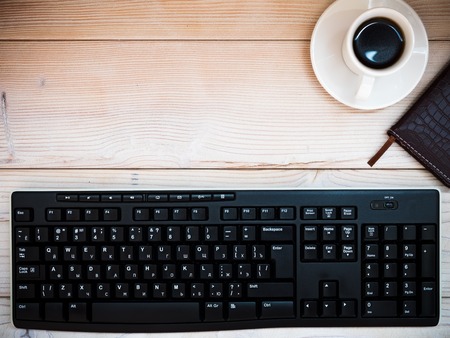 Office table with keyboard, notebook and cup of coffee. View from above