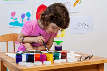 Little girl is drawing with paints and paintbrush.の写真素材