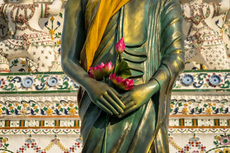 Standing Buddha sculpture wrapped in golden robe, kasaya, with lotus flowers placed in its hands.