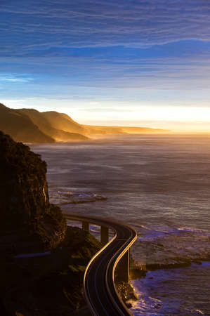 Aerial view of Sea Cliff bridge at sunrise, dusk with sunbeams and sunrays. Australian roads and infrastructure. Sightseeing tourist destination in Stanwell Tops park NSW, Australiaの写真素材