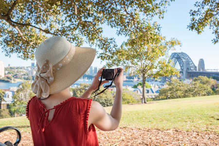 Woman sitting on a bench in a park and looking at Sydney Harbour bridgeの写真素材