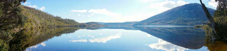 Panorama of beautiful mountain range landscape reflected in smooth water surface of lake on clear dayの写真素材