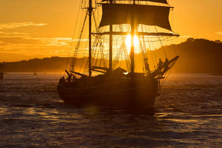 Silhouette of old ship with sails against colorful orange sunset sky on the background