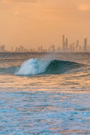 Beautiful big wave with iconic Gold Coast skyscrapers on the background at sunset. Queensland, Australiaの写真素材