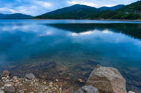 Rock shore and calm water of mountain lake at dusk. Nozori lake, Japan