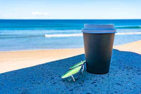 Coffee cup and sunglasses with beach on the background. Summer vacation lifestyle