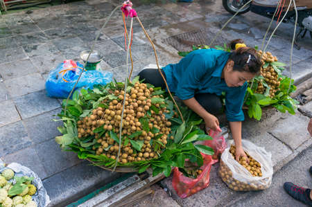 Hanoi, Vietnam - August 21, 2017: Side street morning market in Hanoi. Hawker woman selling fruits from traditional hanging basketsのeditorial素材