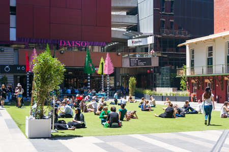 Melbourne, Australia - December 7, 2016: Multinational people relaxing on green lawn at lunch time...
