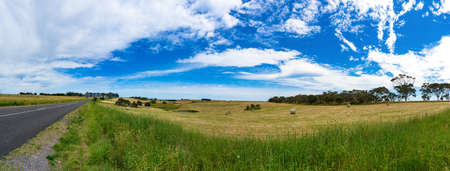 Spectacular panorama of countryside road and field with straw bales on sunny day. Australian rural landscape. Nature backgroundの写真素材