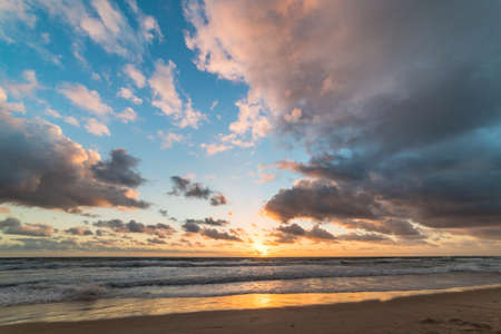 Sunrise on tropical beach with colorful sky and mild waves on sandy shore. Nature background