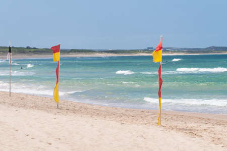 Red and yellow flags on patrolled beach indicating safe to swim area. Water safety and summertime...